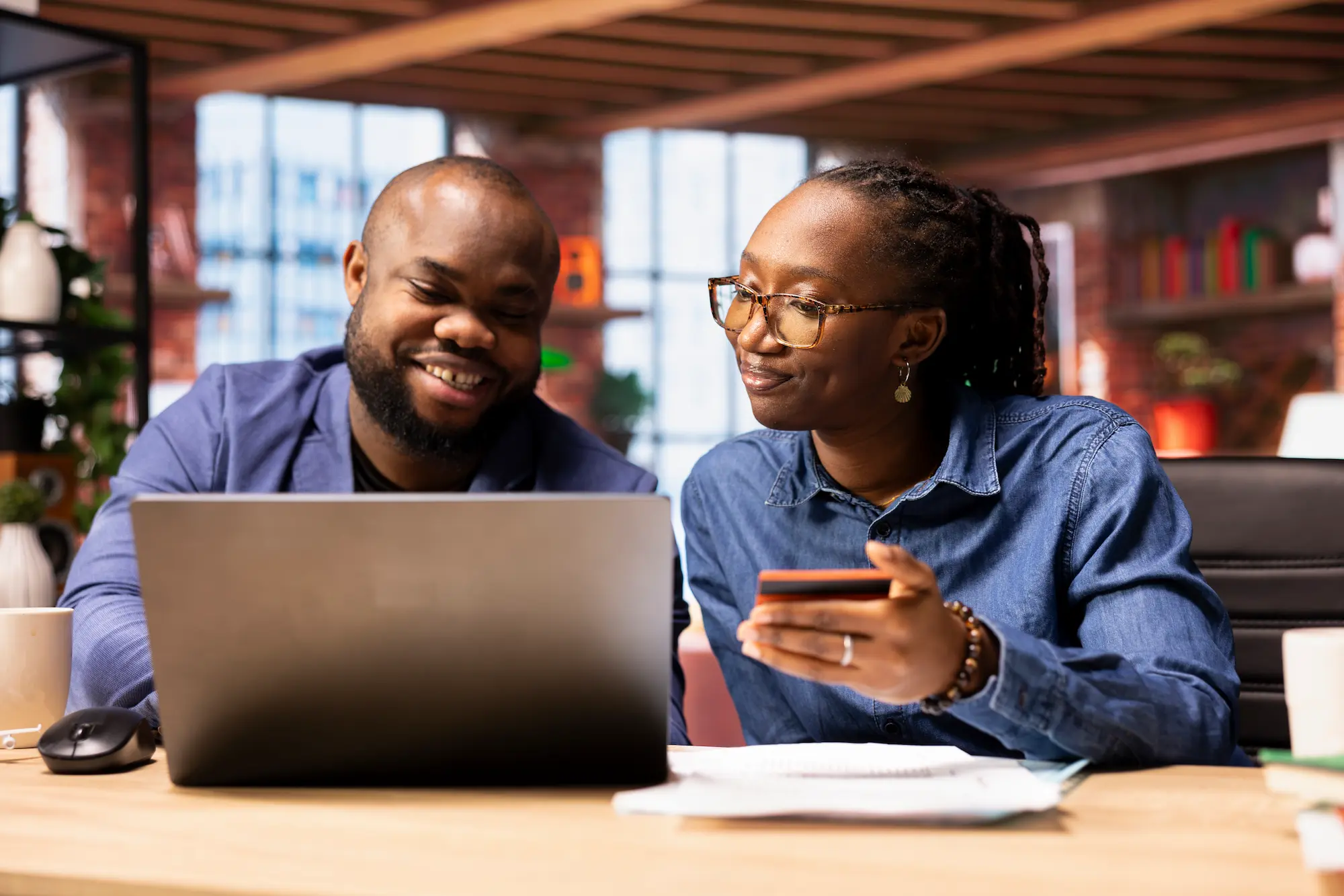 Two colleagues using a laptop and payment card to manage an online business transaction.